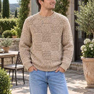 Könnte beinhalten: Ein beigefarbener Langarmpullover mit strukturiertem Schachbrettmuster, Rundhalsausschnitt sowie gerippten Bündchen an Ärmeln und Saum, kombiniert mit einer hellblauen Jeans. Der Pullover zeigt abwechselnde Quadrate aus vertikalen und horizontalen Strickmaschen.