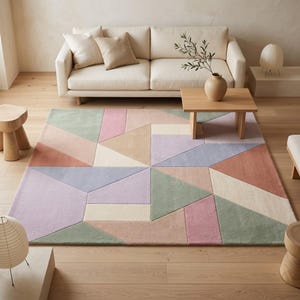 Könnte beinhalten: Ein großer rechteckiger Teppich mit einem geometrischen Muster aus ineinandergreifenden Formen in gedeckten Pastelltönen wie Salbeigrün, Altrosa, Lavendel, Creme und Beige. Der Teppich hat eine weiche Kurzflor-Textur und liegt auf einem hellen Holzboden.