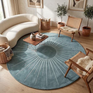 May include: A large, round, blue area rug featuring a central circle with radiating lines that extend toward the outer edge, creating a sunburst pattern. The rug has a soft, textured surface and is positioned on a light-colored wooden floor.