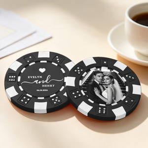 Op de afbeelding: Twee ronde zwart-witte pokerchips. Eén chip bevat een wit hartje, de tekst "EVELYN and HENRY" en de datum "06.06.2026". De andere chip toont een zwart-witfoto van een koppel in trouwkleding op een trap.