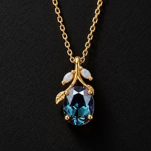 Peut inclure: Un collier doré avec un pendentif orné d'une grande pierre précieuse ovale aux reflets bleu profond et violet. La monture est conçue comme une petite branche avec deux minuscules pierres blanches ovales en forme de feuilles.