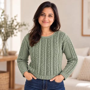 May include: A sage green long-sleeved sweater featuring a vertical cable knit pattern, a round neckline, and ribbed cuffs and hem. The garment is constructed with a textured stitch design that runs throughout the front and sleeves of the piece.