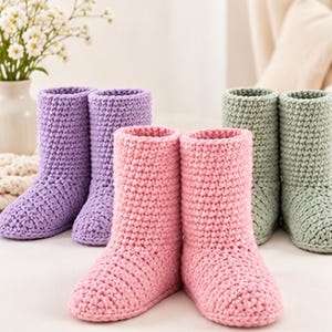 May include: Three pairs of ankle-high crochet boots in solid pastel colors. One pair is light purple, one pair is light pink, and one pair is light green. Each boot features a thick, textured yarn construction with a rounded toe and a straight shaft.