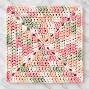 Könnte beinhalten: Ein quadratisches Häkelquadrat im Granny-Square-Stil mit einem melierten Garnmuster in den Farben zartes Rosa, Salbeigrün, Creme und Pfirsich. Das Textil ist mit Stäbchen gearbeitet, die in einem geometrischen Motiv von der Mitte ausgehen.