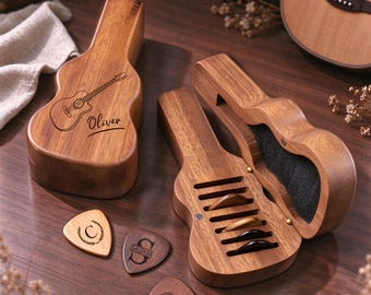 May include: A guitar-shaped wooden box with the name Oliver engraved on the lid, alongside an open version containing three guitar picks. Three additional wooden guitar picks with engraved designs are placed on the surface nearby.