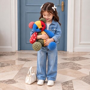 May include: A plush teddy bear constructed from various fabric patches in red, blue, yellow, and green, featuring a mix of solid colors, gingham checks, and floral patterns. The bear has round black eyes and a small brown nose, held in a hug.