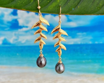 May include: Gold earrings with a leaf design and black pearl drops. The earrings are hanging from a green leaf.