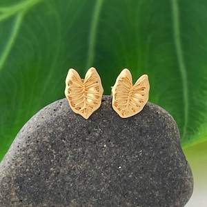 May include: A pair of gold leaf-shaped earrings. The earrings are small and delicate, and they have a natural, organic look.