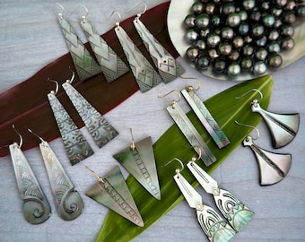May include: A collection of 10 pairs of earrings made from mother of pearl shell. The earrings are in various shapes and sizes, including triangles, rectangles, and teardrop shapes. The earrings are decorated with intricate designs and patterns. Some of the earrings have a silver hook, while others have a gold hook.