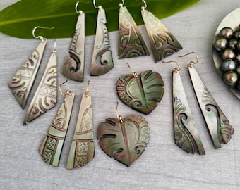 May include: A set of six pairs of earrings made from carved mother-of-pearl shell. The earrings are in the shapes of triangles, hearts, and leaves. The earrings are a dark green and brown color.