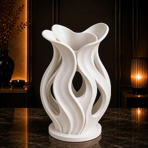 May include: A white vase with a complex, sculptural design featuring multiple vertical, wave-like curved panels that create an open, airy structure. The object has a smooth, matte finish and stands on a circular base with a wide, flared opening.