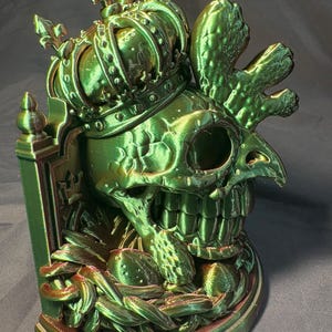 Front-right view of King of the Coop, a crowned rooster-inspired skull sculpture in glossy green and gold tri-color silk PLA. The printed artwork has feather details, a decorative back panel and a flat display base.