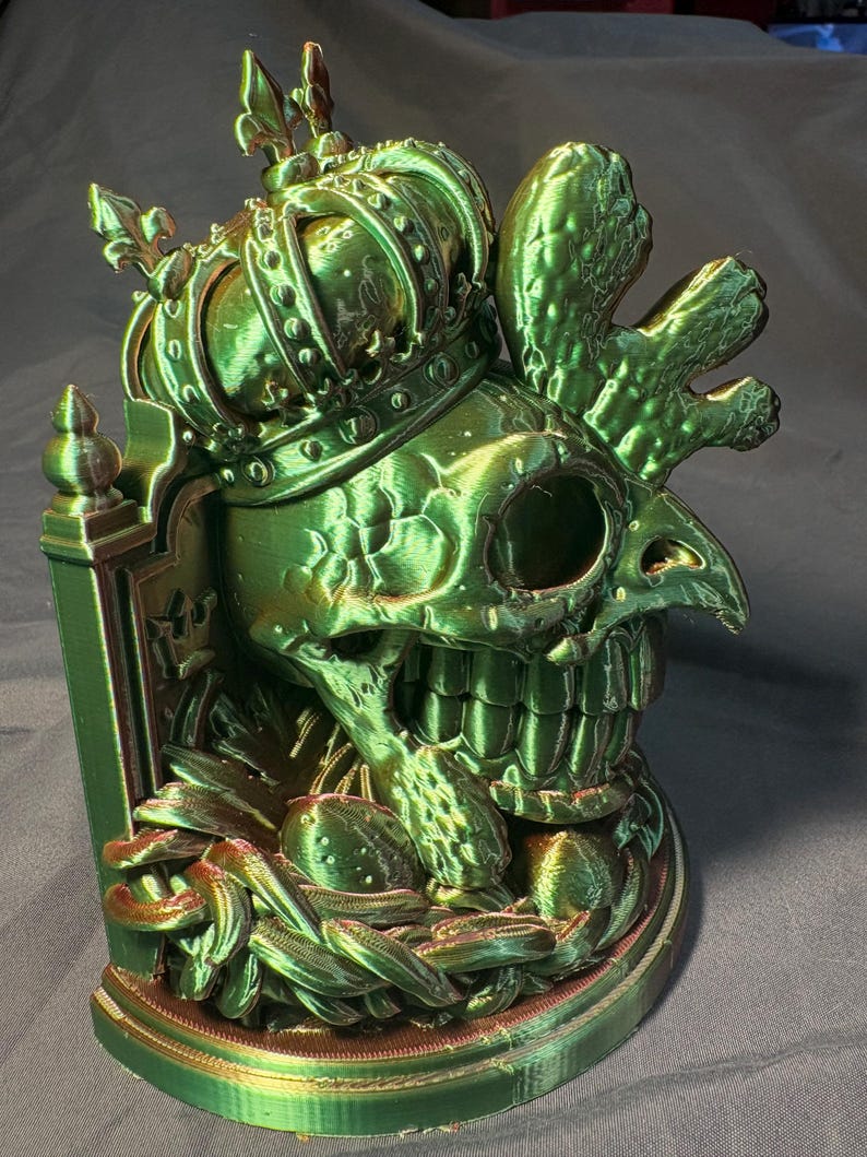 Front-right view of King of the Coop, a crowned rooster-inspired skull sculpture in glossy green and gold tri-color silk PLA. The printed artwork has feather details, a decorative back panel and a flat display base.