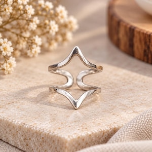 May include: A silver-toned metal ring featuring a geometric, open-work design with two symmetrical, pointed chevron-like shapes that meet in the center, creating a hollow, angular silhouette with a smooth, polished finish throughout the band.