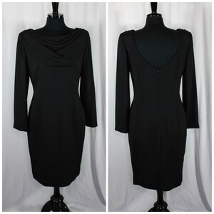 Puede incluir: Vestido negro con mangas largas y cuello drapeado, exhibido en un maniquí. La parte trasera del vestido presenta un escote en la espalda bajo y una cremallera. El vestido es hasta la rodilla y está hecho de tela oscura.