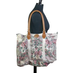 Könnte beinhalten: Eine große, floral gemusterte Tragetasche mit braunen Ledergriffen. Die Tasche ist aus einem Patchwork-Stoff mit einem Blumendesign in den Farben Rosa, Grün und Weiß.
