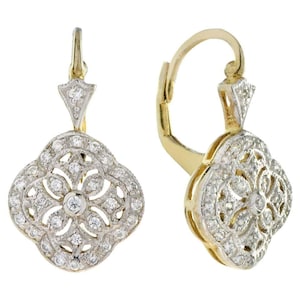 May include: A pair of gold drop earrings featuring a clover-shaped design with intricate filigree metalwork and small clear stones embedded throughout the surface. The earrings are suspended from a gold lever-back mechanism with a triangular accent.