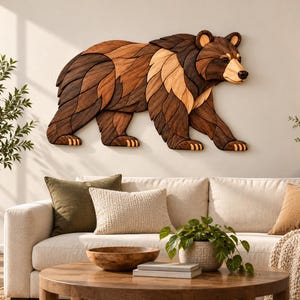 Könnte beinhalten: Eine Wandskulptur in Form eines Bären, gefertigt aus geschichteten Holzteilen in verschiedenen Braun- und Beigetönen. Der Bär ist im Gehen von der Seite dargestellt und weist deutliche Holzmaserungen sowie glatte, geschwungene Kanten auf.