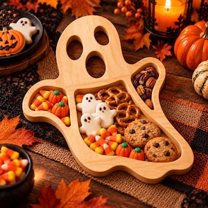 May include: A light-colored wooden serving tray shaped like a ghost with multiple internal compartments. The tray is filled with various snacks including ghost-shaped cookies, chocolate chip cookies, pretzels, candy corn, and small pumpkin candies.