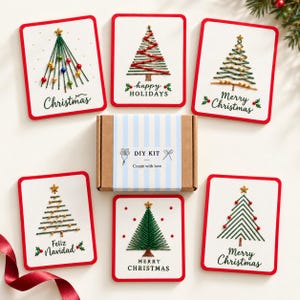 Puede incluir: Una caja de kit de manualidades con una etiqueta de rayas azul claro que dice DIY KIT Create with love, rodeada de seis tarjetas de felicitación blancas con diseños de árboles de Navidad bordados, estrellas doradas, cuentas y texto festivo.