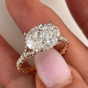 Peut inclure: Une bague avec un diamant taille ovale montée sur un anneau en or rose au design à double branche. L'anneau présente de petits diamants pavés sur les côtés et un motif texturé rappelant une vigne, avec un sertissage à quatre griffes.