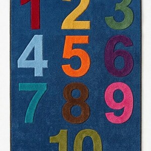 May include: A rectangular blue rug featuring the numbers one through ten in a grid layout. The numbers are displayed in various colors including red, yellow, green, light blue, orange, purple, teal, brown, pink, and olive green, with a textured finish.