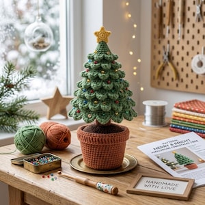 Könnte beinhalten: Ein gehäkelter grüner Weihnachtsbaum mit einem gelben Stern als Spitze, verziert mit kleinen bunten Perlen, in einem braunen gehäkelten Topf. Der Baum steht auf einem Holztisch neben Wollknäueln, einer Dose mit Perlen und einem Anleitungsblatt.