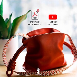 Puede incluir: Un bolso de mano color naranja óxido con acabado liso y una correa ancha tejida con un patrón de chevrón en rojo, blanco y marrón. El bolso incluye un detalle de nudo en un lateral. El texto dice PDF INSTANT DOWNLOAD y VIDEO TUTORIAL.