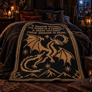May include: A black and gold knit blanket featuring a large dragon illustration, star accents, and mountain motifs at the bottom. The text reads: A DRAGON WITHOUT ITS RIDER IS A TRAGEDY. A RIDER WITHOUT THEIR DRAGON IS DEAD. The design has a border.
