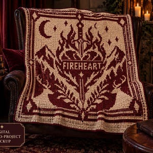 May include: A rectangular crochet blanket featuring a two-tone design in deep burgundy and cream. The pattern displays a central sword, flames, mountains, and deer silhouettes, with the word FIREHEART centered in a banner across the middle.