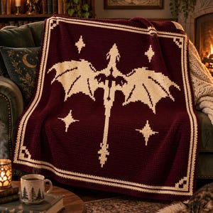 May include: A deep burgundy crochet blanket featuring a large, cream-colored dragon silhouette centered on the fabric. The design includes four four-pointed stars surrounding the dragon and a decorative cream-colored border along the edges.