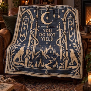 May include: A dark blue and cream crochet blanket featuring a central crescent moon, stars, and the text YOU DO NOT YIELD. The design includes two upright swords, a mountain landscape, and two wolves facing each other, all framed by an arched border.