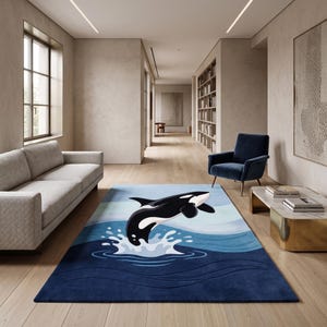 Puede incluir: Una alfombra rectangular que presenta una ilustración gráfica de una orca negra y blanca saltando sobre olas oceánicas azules estilizadas. El diseño incluye tonos de azul en capas y salpicaduras de agua blancas sobre una base azul oscuro.