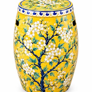 Puede incluir: Un taburete de jardín de cerámica en forma de barril con un esmalte amarillo brillante. La superficie presenta un diseño pintado a mano de ramas de árbol azul oscuro con flores blancas y hojas verdes. Un borde decorativo azul y blanco rodea la parte superior.