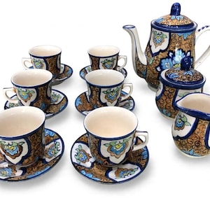 May include: A ceramic tea set featuring a teapot, a lidded sugar bowl, a creamer, and six cups with matching saucers. Each piece is decorated with a brown and blue floral pattern on a cream background, accented by dark blue painted rims.