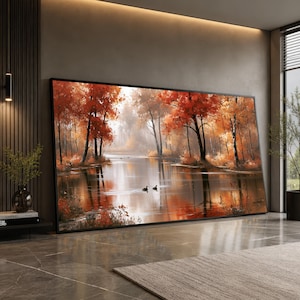 Puede incluir: Una gran pieza de arte mural rectangular enmarcada que presenta una pintura de paisaje de un lago tranquilo rodeado de árboles con follaje otoñal de color naranja y rojo vibrante. Dos pequeñas aves oscuras nadan en el agua, reflejando los árboles.