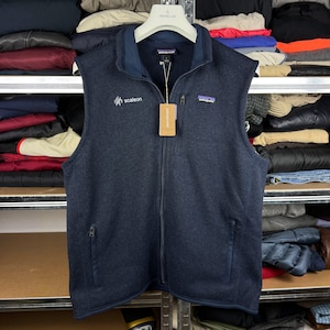 Könnte beinhalten: Eine dunkelblaue Patagonia Fleeceweste mit durchgehendem Frontreißverschluss, Stehkragen und zwei Reißverschlusstaschen. Auf der Brust befindet sich ein kleines Patagonia-Logo sowie ein weißes Sticklogo mit dem Schriftzug scaleon.