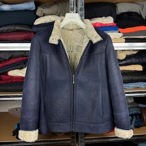 Puede incluir: Una chaqueta azul marino oscuro con exterior texturizado y un forro grueso de piel de oveja color crema. La chaqueta cuenta con una cremallera frontal completa, un cuello ancho doblado y mangas largas con puños de piel de oveja a juego.