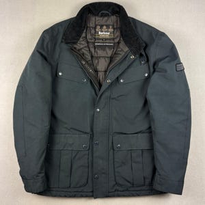 Puede incluir: Una chaqueta Barbour International de color gris carbón oscuro con cuello de pana, forro interior acolchado marrón y cuatro bolsillos delanteros con cierre de corchetes. La chaqueta incluye cremallera frontal, tapeta con corchetes y un parche.