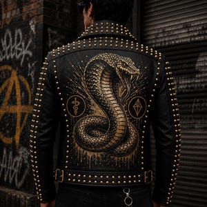 Può includere: Una giacca in pelle nera con borchie metalliche dorate su colletto, spalle e maniche. Il retro presenta una grande e dettagliata grafica dorata di un cobra avvolto a bocca aperta, affiancato da due piccoli simboli circolari.