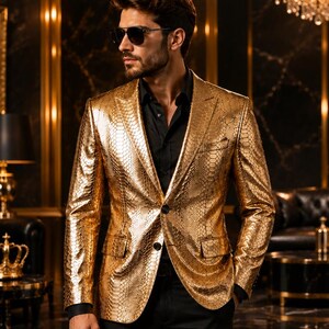 Puede incluir: Un blazer dorado metálico con un patrón texturizado de piel de serpiente, solapas de muesca, dos botones frontales y dos bolsillos con solapa, usado sobre una camisa negra abotonada y pantalones negros, con gafas de sol oscuras.