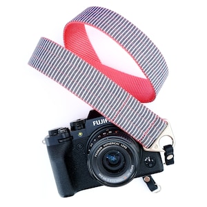 May include: A black camera with a red and blue striped camera strap. The camera lens says "FUJIFILM" and "SUPER EBC 16mm 1:2.8 R WR"