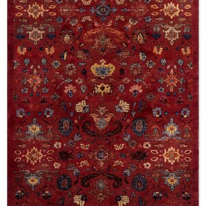 May include: A rectangular area rug featuring a deep red background with a repeating pattern of intricate floral and geometric motifs in shades of blue, gold, cream, and dark brown, arranged in a symmetrical layout across the entire surface.
