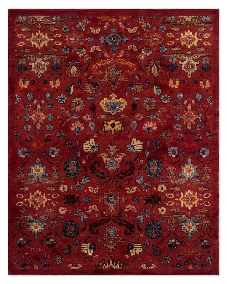May include: A rectangular area rug featuring a deep red background with a repeating pattern of intricate floral and geometric motifs in shades of blue, gold, cream, and dark brown, arranged in a symmetrical layout across the entire surface.