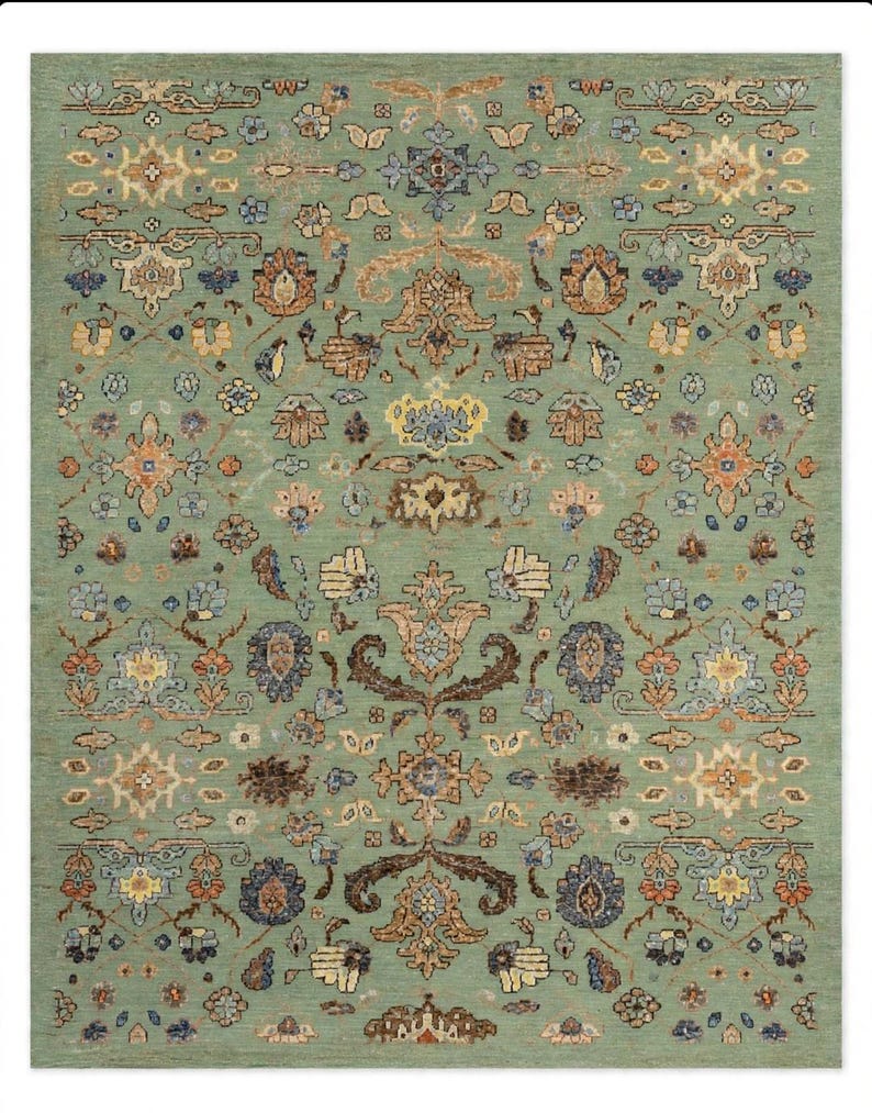 May include: A rectangular area rug featuring a sage green background with a repeating symmetrical pattern of floral and botanical motifs in shades of rust orange, navy blue, cream, and brown, creating a dense and intricate decorative design.