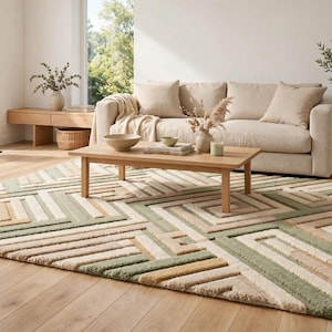 May include: A rectangular area rug featuring a geometric pattern of raised, textured lines in shades of sage green, cream, and tan. The design consists of interlocking squares and rectangular shapes, creating a multi-dimensional surface texture.