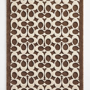 May include: A rectangular rug featuring a brown base with a repeating cream-colored pattern of interlocking C-shaped logos. The design consists of a dense, tufted texture that creates a raised, tactile surface across the entire mat.