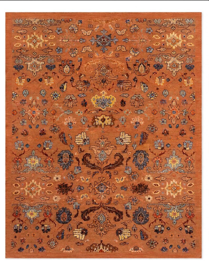 May include: A rectangular area rug featuring a deep burnt orange background with a repeating pattern of intricate floral and botanical motifs in shades of navy blue, light blue, cream, yellow, and dark brown, arranged in a symmetrical layout.