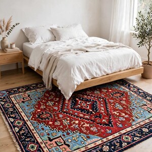 May include: A rectangular area rug featuring a central dark red diamond medallion surrounded by intricate geometric patterns in shades of light blue, navy, pink, and green, finished with a dark navy border and short white fringe on the ends.