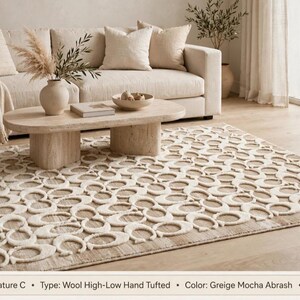 May include: A rectangular wool high-low hand-tufted rug featuring a repeating Signature C pattern in greige and mocha abrash colors. The rug measures 5x8 ft and displays a textured surface with raised cream-colored letter C motifs.